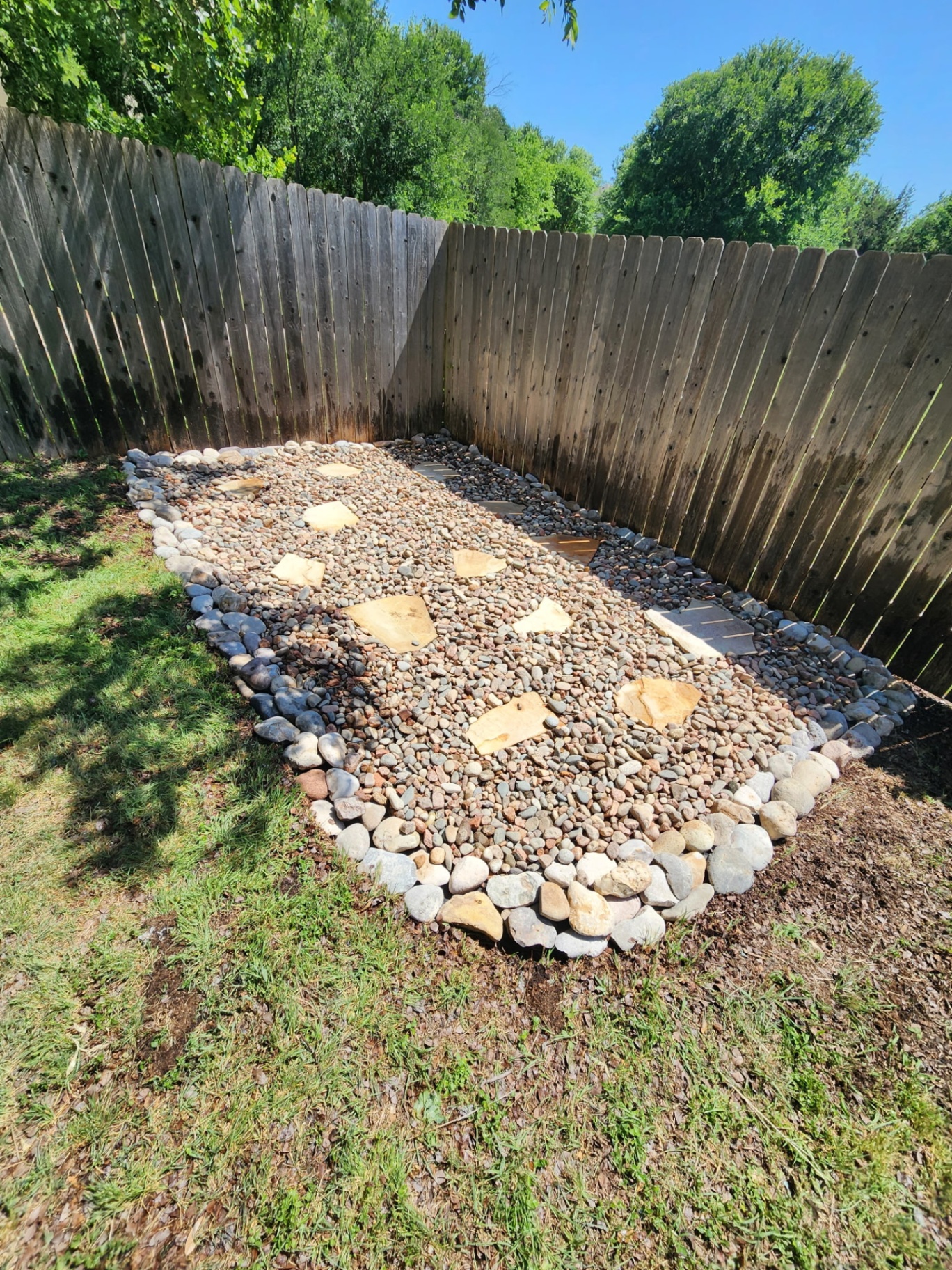 Custom river-rock drainage bed with flagstone path along a backyard fence line